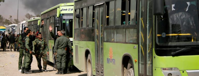 Members of Syrian forces of President Bashar al Assad stand next to buses carrying rebels and their families before they are evacuated, at Harasta highway outside Jobar, in Damascus