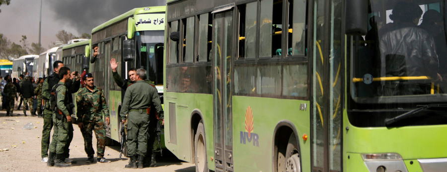 Members of Syrian forces of President Bashar al Assad stand next to buses carrying rebels and their families before they are evacuated, at Harasta highway outside Jobar, in Damascus
